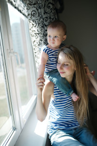 A mother and toddler look out a window.