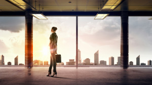 A business woman stands in front of office windows with sunlight streaming in.